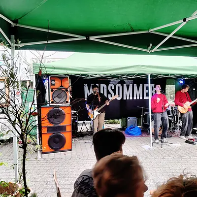 Et band spiller live under et grønt telt med anlægget ved siden af scenen.